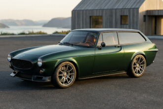 Une Volvo P1800 Norrsken restomod vert foncé, garée devant une maison moderne en bois avec un paysage lacustre.