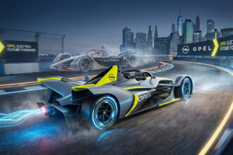 Deux monoplaces de Formule E, dont une Opel, sur une piste urbaine illuminée la nuit. La voiture Opel laisse une traînée bleue électrique.