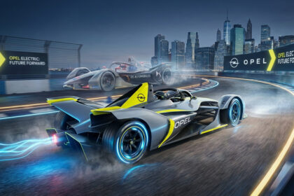 Deux monoplaces de Formule E, dont une Opel, sur une piste urbaine illuminée la nuit. La voiture Opel laisse une traînée bleue électrique.