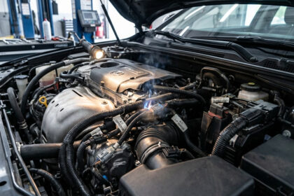 Vue rapprochée du moteur d'une voiture en atelier avec des étincelles et de la fumée sur des câbles de climatisation.