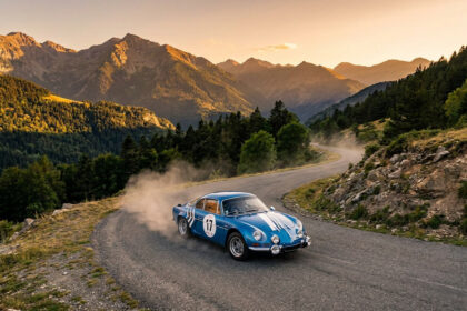 Alpine A110 bleue n°17 sur route de montagne sinueuse, levant de la poussière. Coucher de soleil sur les Pyrénées boisées.