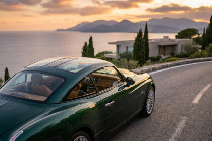 Une Morgan Midsummer Coupé vert foncé avec un toit vitré panoramique garée sur une route côtière au coucher du soleil.