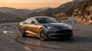 Une Aston Martin Vanquish 25 grise garée sur une route sinueuse en montagne au coucher du soleil.