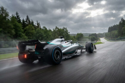 Une voiture de course Mercedes roule sur la piste mouillée du circuit de Spa-Francorchamps sous un ciel nuageux.