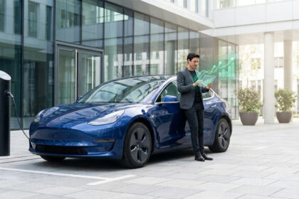 Un homme d'affaires consulte des données financières sur une tablette devant une Tesla en charge.