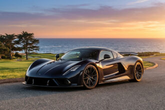 La supercar noire Hennessey Blackbird stationnée sur une route côtière au coucher du soleil.
