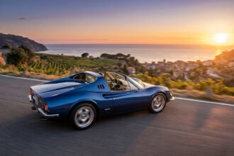 Une voiture de sport bleue Touring Superleggera Veloce 12 Aperta roulant sur une route côtière au coucher du soleil.