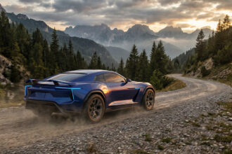 Une Toyota Celica bleue moderne roulant sur un chemin de terre en montagne au coucher du soleil.