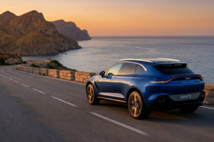 Aston Martin DBX707 bleu roulant sur une route côtière au coucher du soleil.