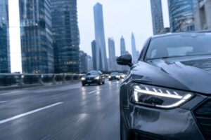 Une voiture Audi circulant sur une route urbaine avec des gratte-ciel en arrière-plan sous un ciel gris.