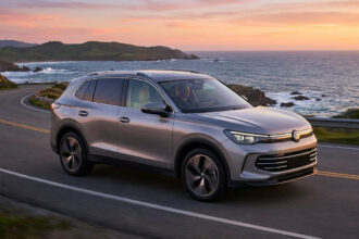 Un SUV Volkswagen argenté roulant sur une route côtière sinueuse au coucher du soleil.